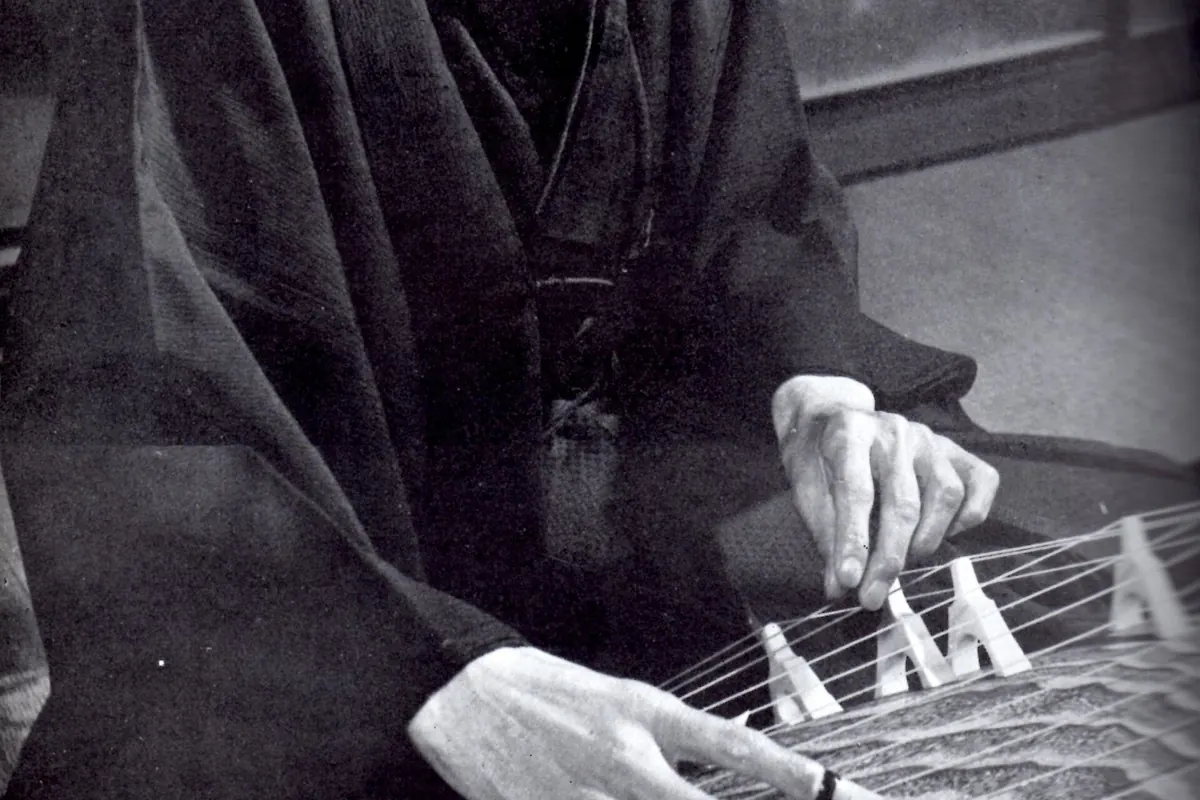 Close-up of a koto player's right hand wearing finger picks beside the movable bridges, from a black-and-white photograph of Michio Miyagi